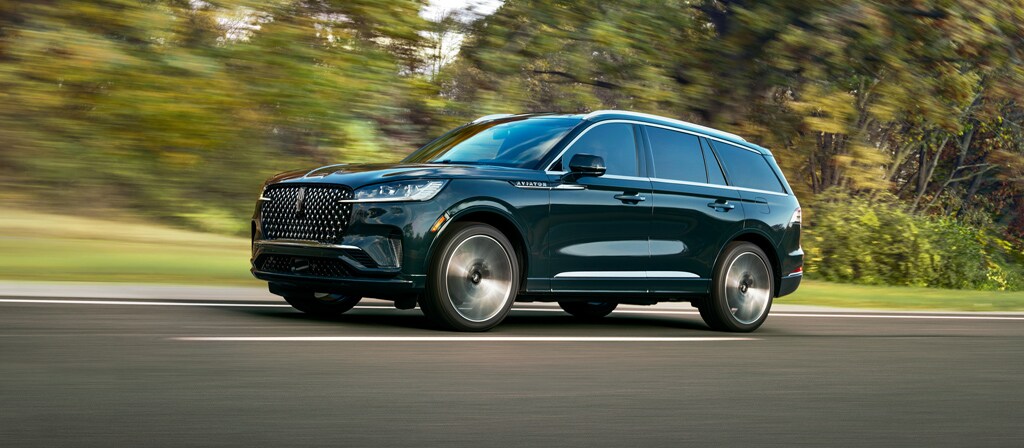 A 2027 Lincoln Aviator® Black Label® is being driven in a lush countryside