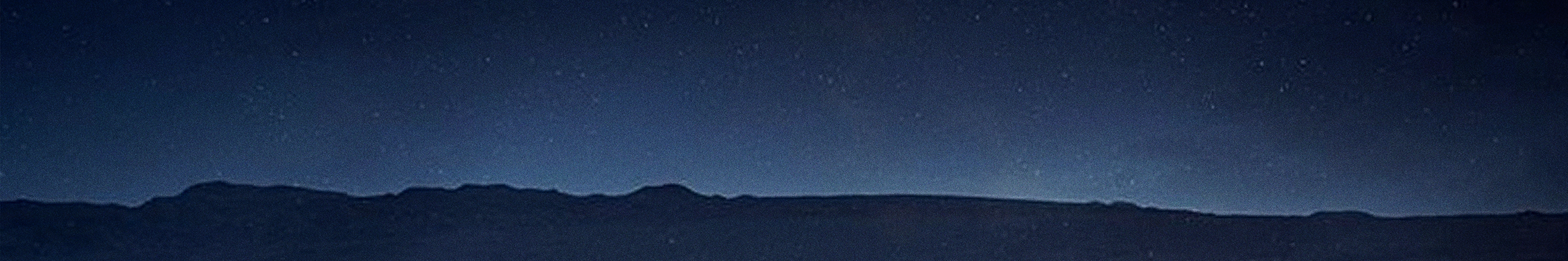 A dark blue night sky, filled with stars, hangs over the silhouette of a distant mountain range