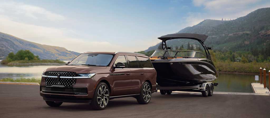 A 2027 Lincoln Navigator® Black Label™ model has a boat hitched up by the water