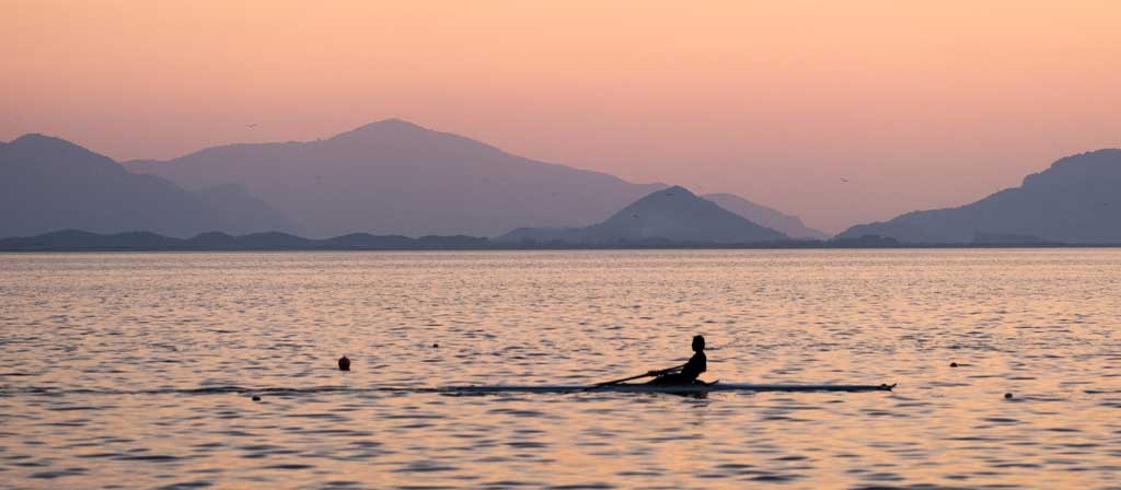 A person rows a scull boat on the ocean in the morning