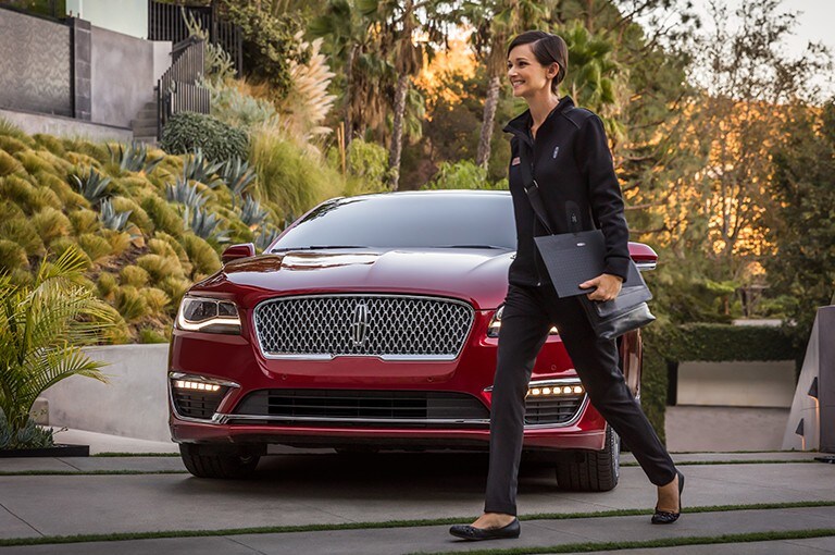 A woman walking in front of a red Lincoln vehicle