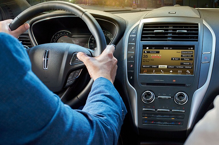 A pair of hands grip the steering wheel of a Lincoln vehicle
