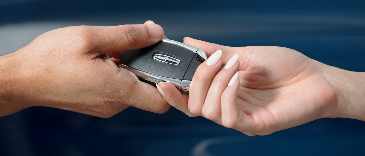 Salesperson handing key fob of a new Lincoln to customer