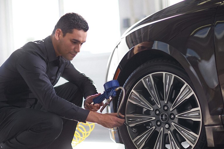 A Lincoln service technician is shown measuring the tire pressure of a Lincoln vehicle as part of a 200 point inspection