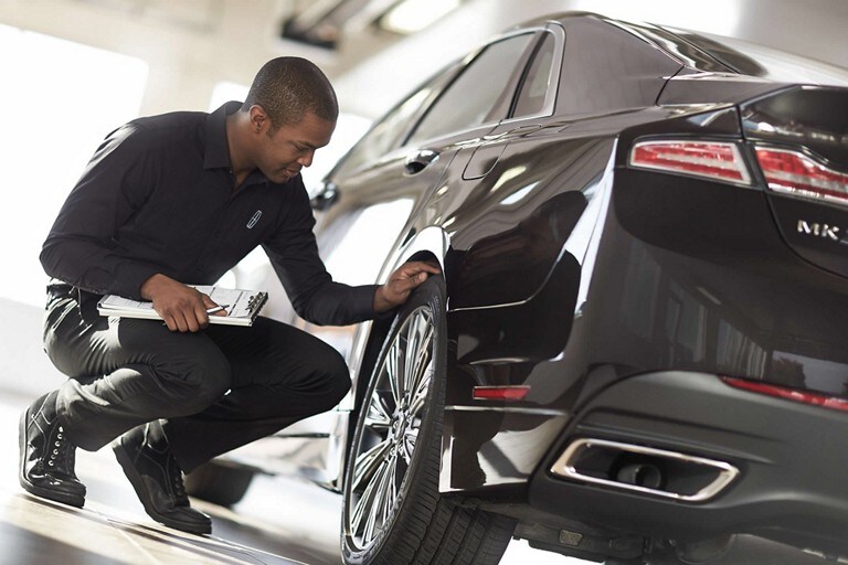 A Lincoln service technician is shown inspecting the tire tread quality of a Lincoln M K Z