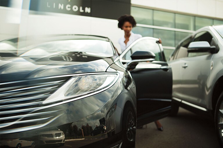 A customer is shown opening the door of a Lincoln vehicle at a dealership