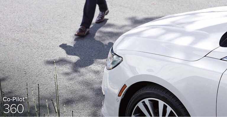 A white Lincoln vehicle stopping in front of a pedestrian which demonstrates Pre Collision Assist with Automatic Braking which is part of Co Pilot 3 60