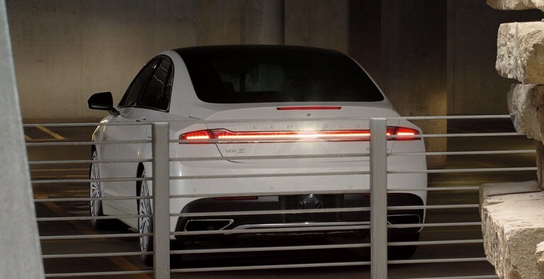 A white Lincoln M K Z backing up in a parking garage demonstrating the Forward and Reverse Sensing Systems feature