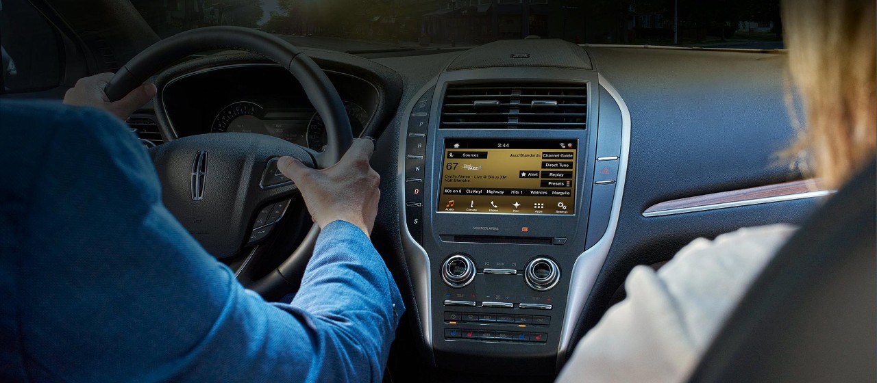 Couple in a Lincoln looking at the Sirius XM interface on the consul.