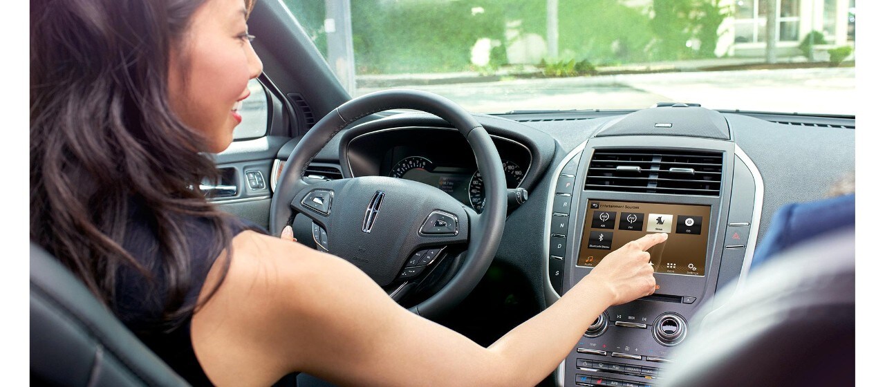 A woman sitting in a Lincoln touches the SiriusXM radio touch-screen button