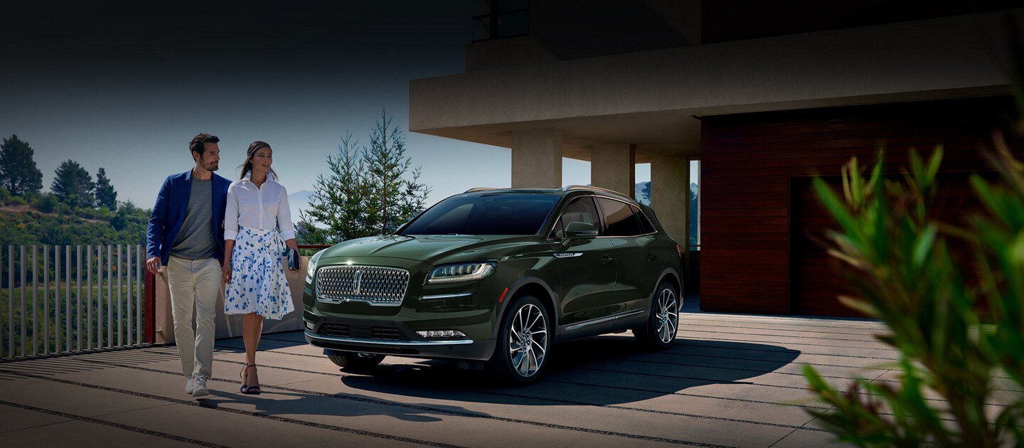 A 2023 Lincoln Nautilus SUV shown in the Gilded Green exterior colour is parked in the driveway of a modern hillside home