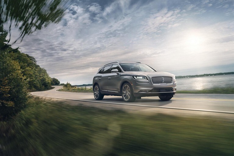 A 2023 Lincoln Nautilus SUV being driven down a lake-side road