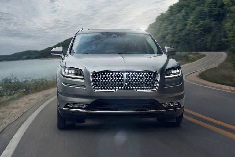 The 2023 Lincoln Nautilus SUV is being driven around a curve on a lake-side road