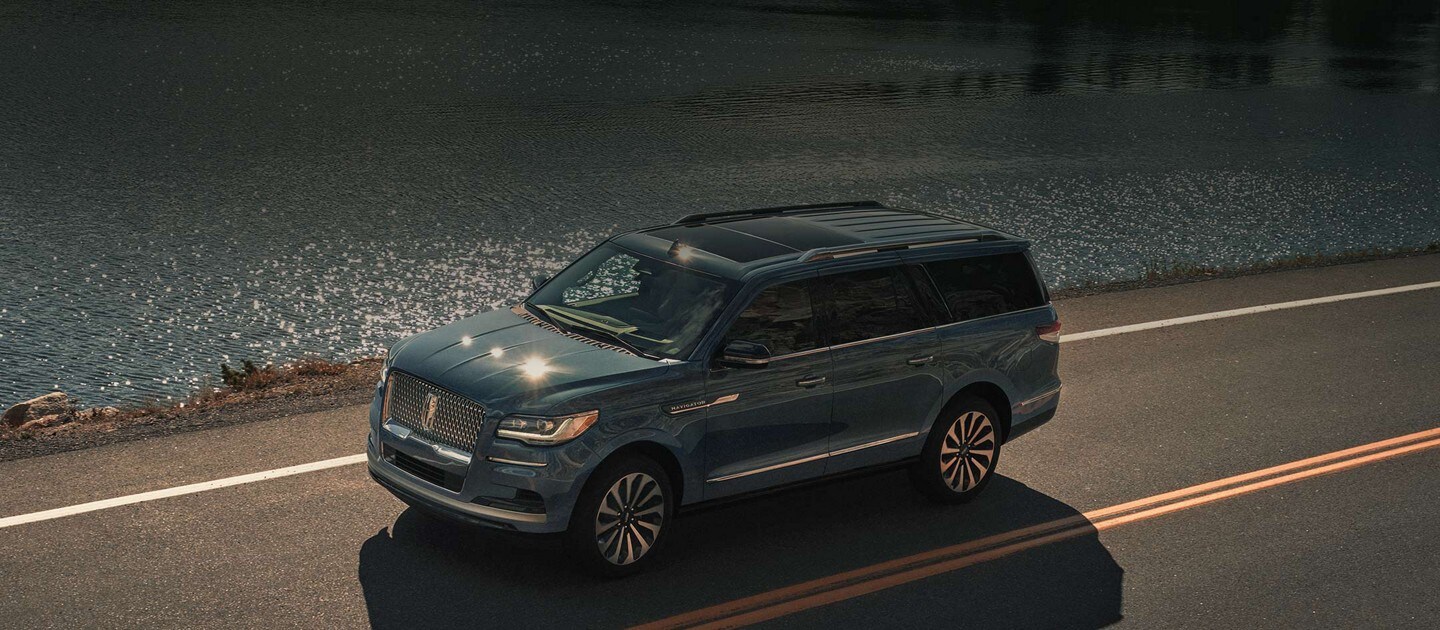 A 2023 Lincoln Navigator® SUV is being driven along a lake up in the mountains