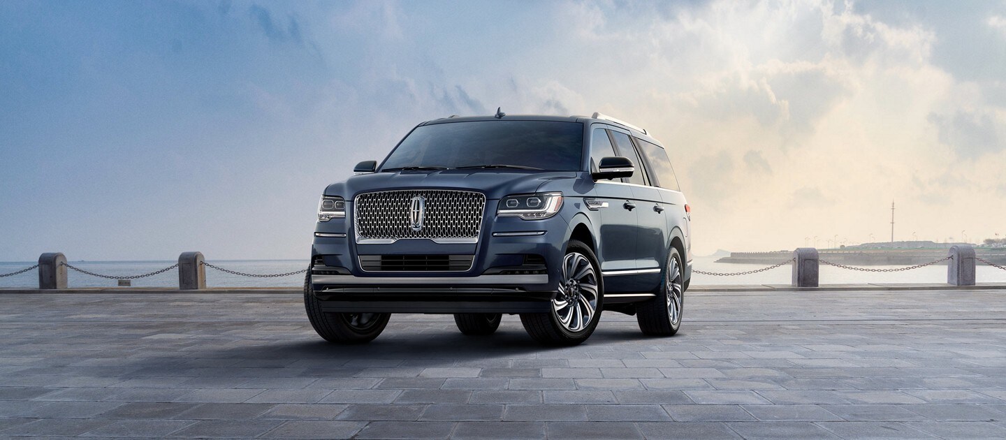 A 2023 Lincoln Navigator® Reserve L model SUV in Ocean Drive Blue is parked near a bay beneath a cloudy sky