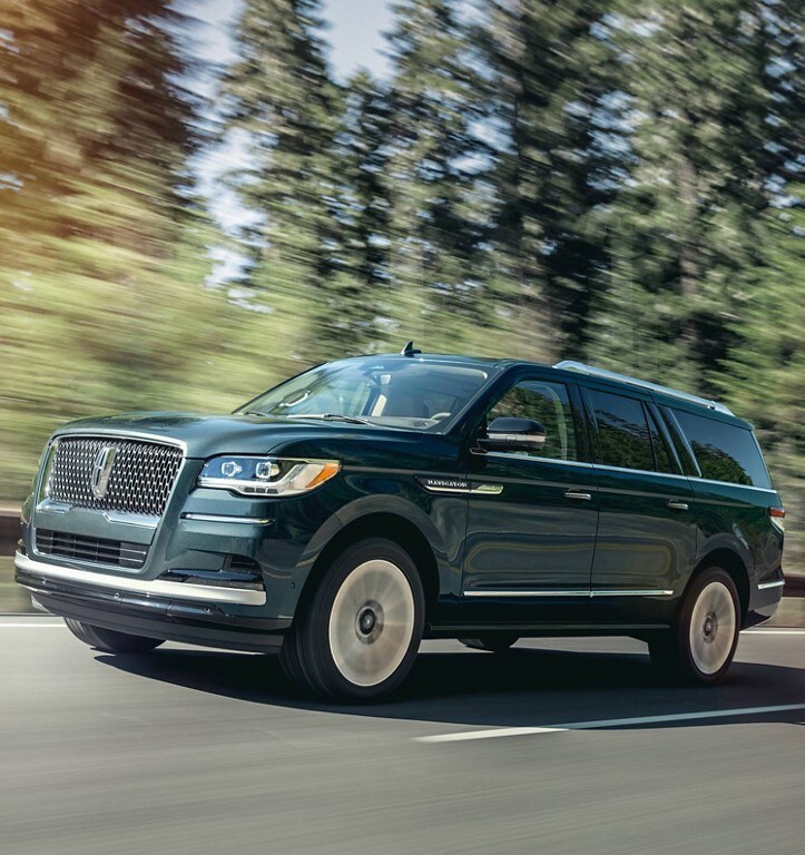 A 2024 Lincoln Navigator in Flight Blue is being driven up an incline surrounded by greenery