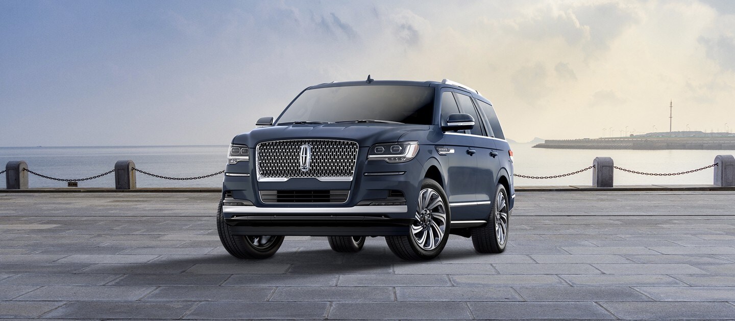 A 2024 Lincoln Navigator Reserve model SUV in Flight Blue is parked near a bay beneath a cloudy sky