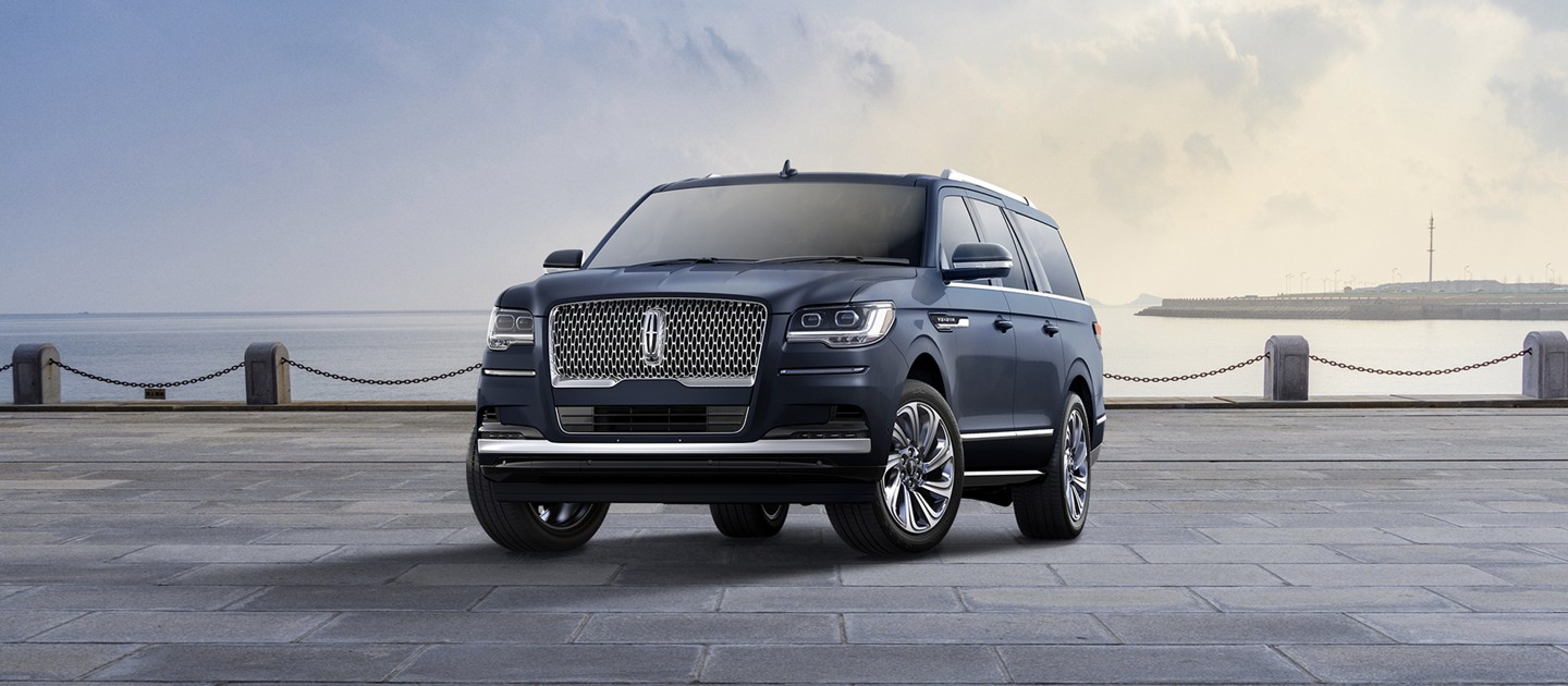 A 2024 Lincoln Navigator Reserve L model SUV in Flight Blue is parked near a bay beneath a cloudy sky