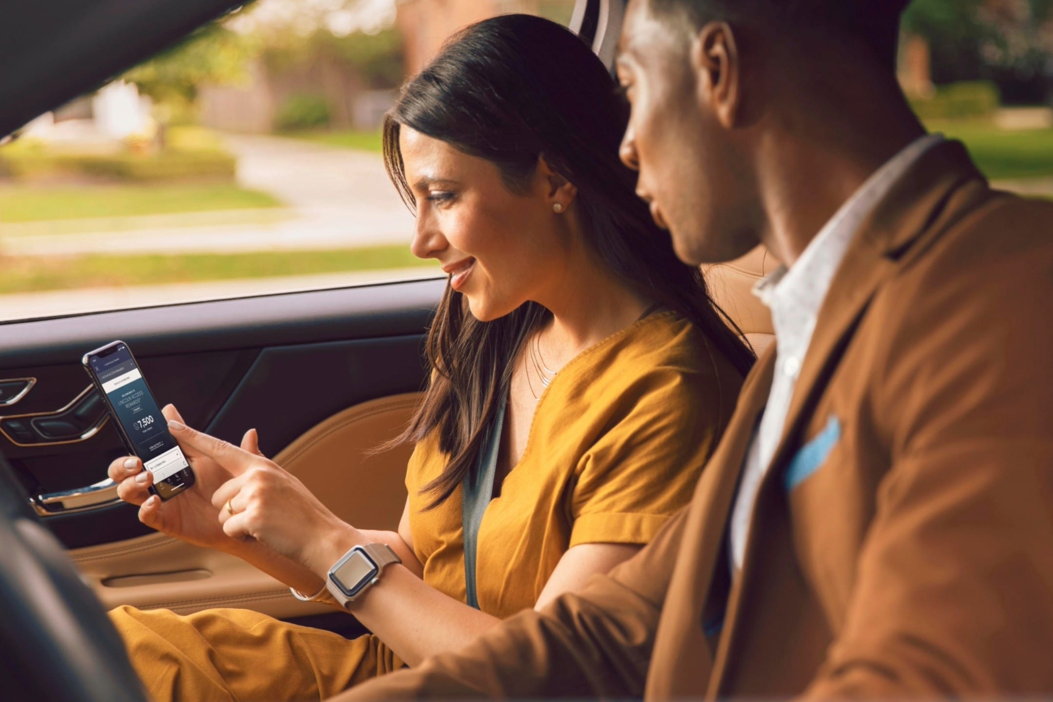 A woman showing a man her Lincoln Rewards on her smartphone.