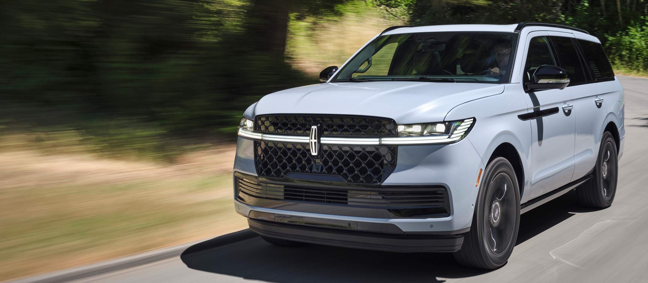 A 2025 Lincoln Navigator with the Available Jet Appearance Package is being driven on a country road