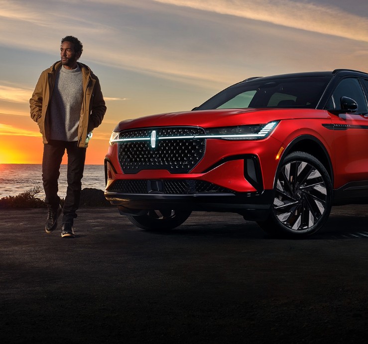 A man standing outside a Lincoln Nautilus parked near a body of water.