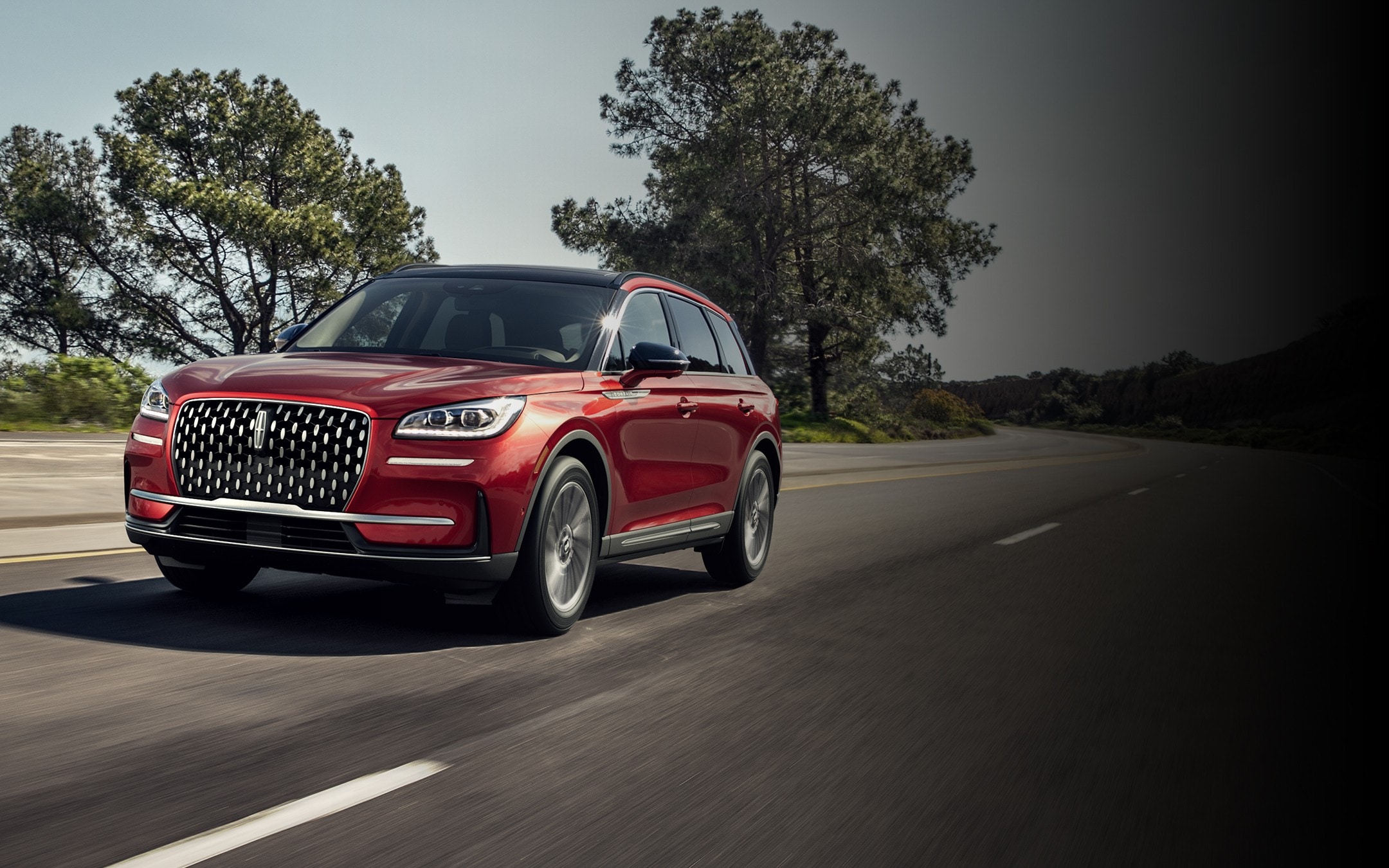 A 2025 Lincoln Corsair in the Red Carpet exterior colour is being driven on a country road