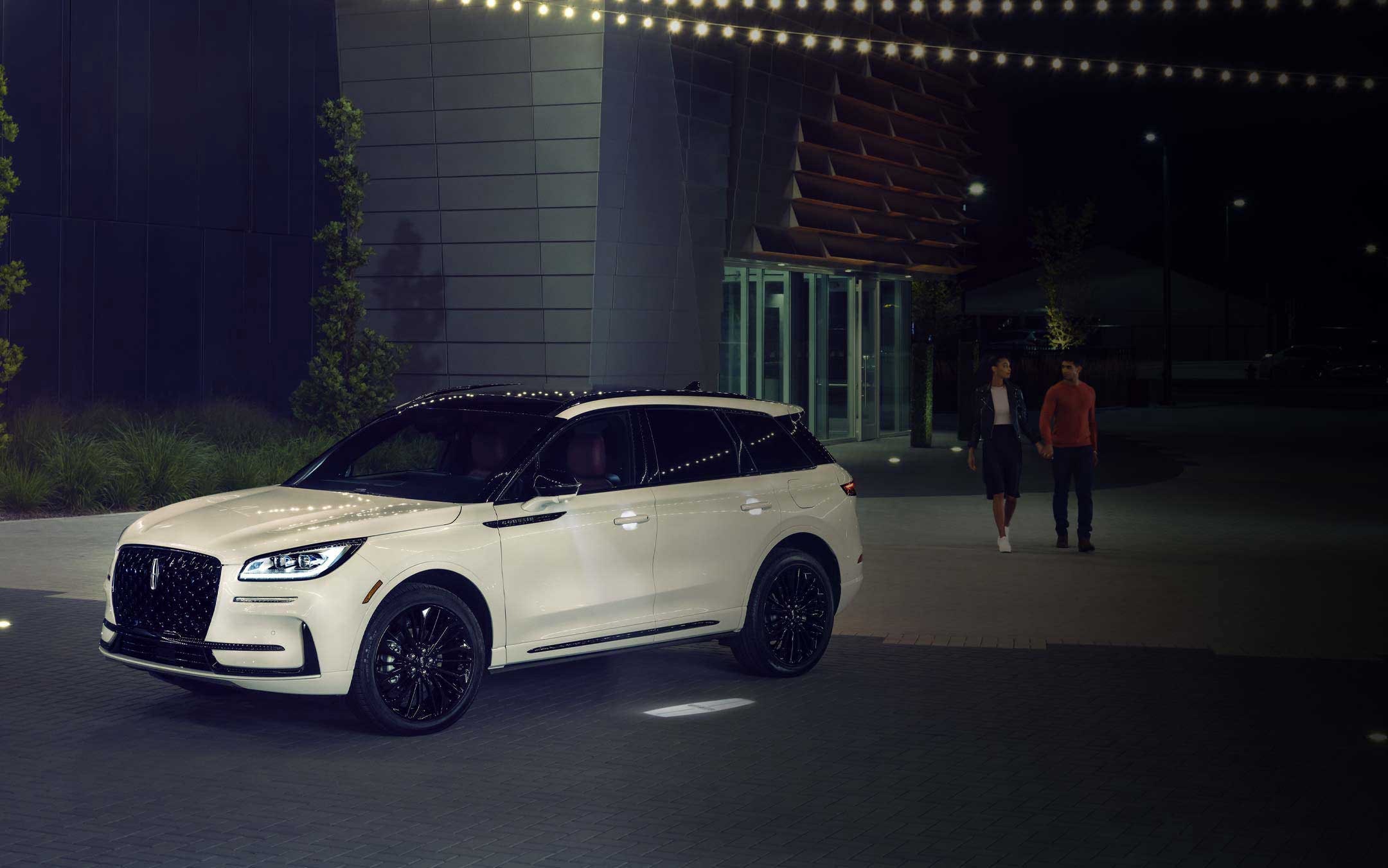 A couple approaches a 2026 Lincoln Corsair SUV as the Lincoln Embrace illumination guides the way