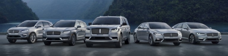 Silver Lincoln Vehicles spread out in a fan formation in front of mountains. 