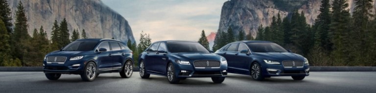 Various 2018 and 2019 Lincoln vehicles in grey and silver parked on wooden bridge in front of water and mountains