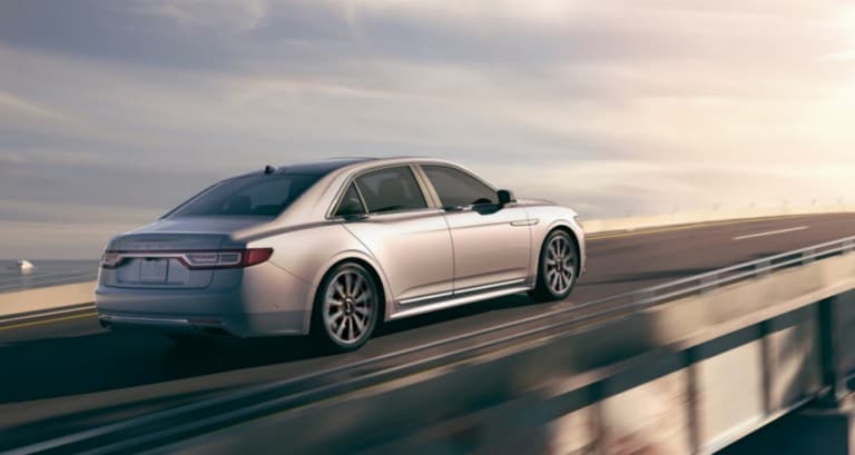 2019 Lincoln Continental in Ingot Silver driving on bridge above ocean towards sunrise