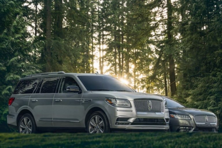 2018 Lincoln Navigator and Continental in Ingot Silver parked on grass near tall trees
