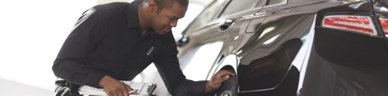 Worker checking tires of 2016 Lincoln M K Z in Infinite Black parked indoors