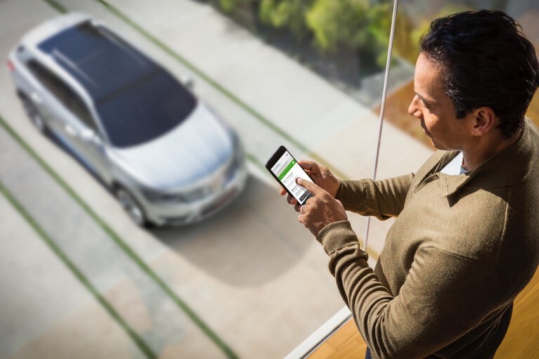 Man using phone next to large window with Lincoln vehicle seen on driveway below