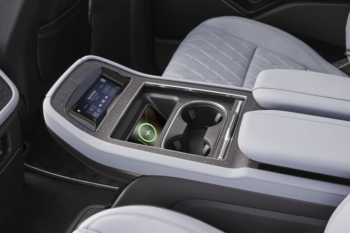 A phone charges on a wireless charging pad in the second row console of a 2025 Lincoln Black Label Navigator.