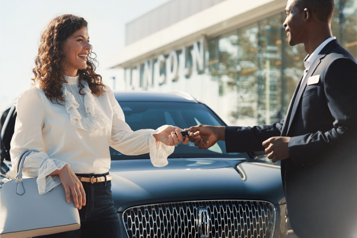 A man is handing keys to a woman in front of a Lincoln SUV