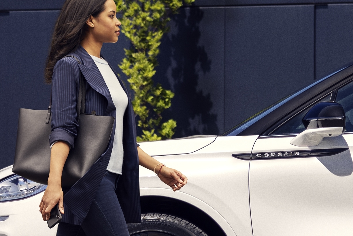 A woman is shown walking to a Lincoln Corsair SUV while holding a mobile device.