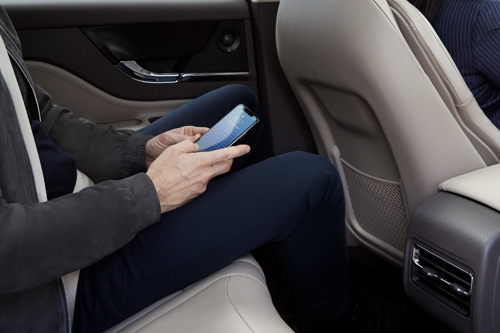 A person is in the second-row seat of a Lincoln vehicle using their mobile device.