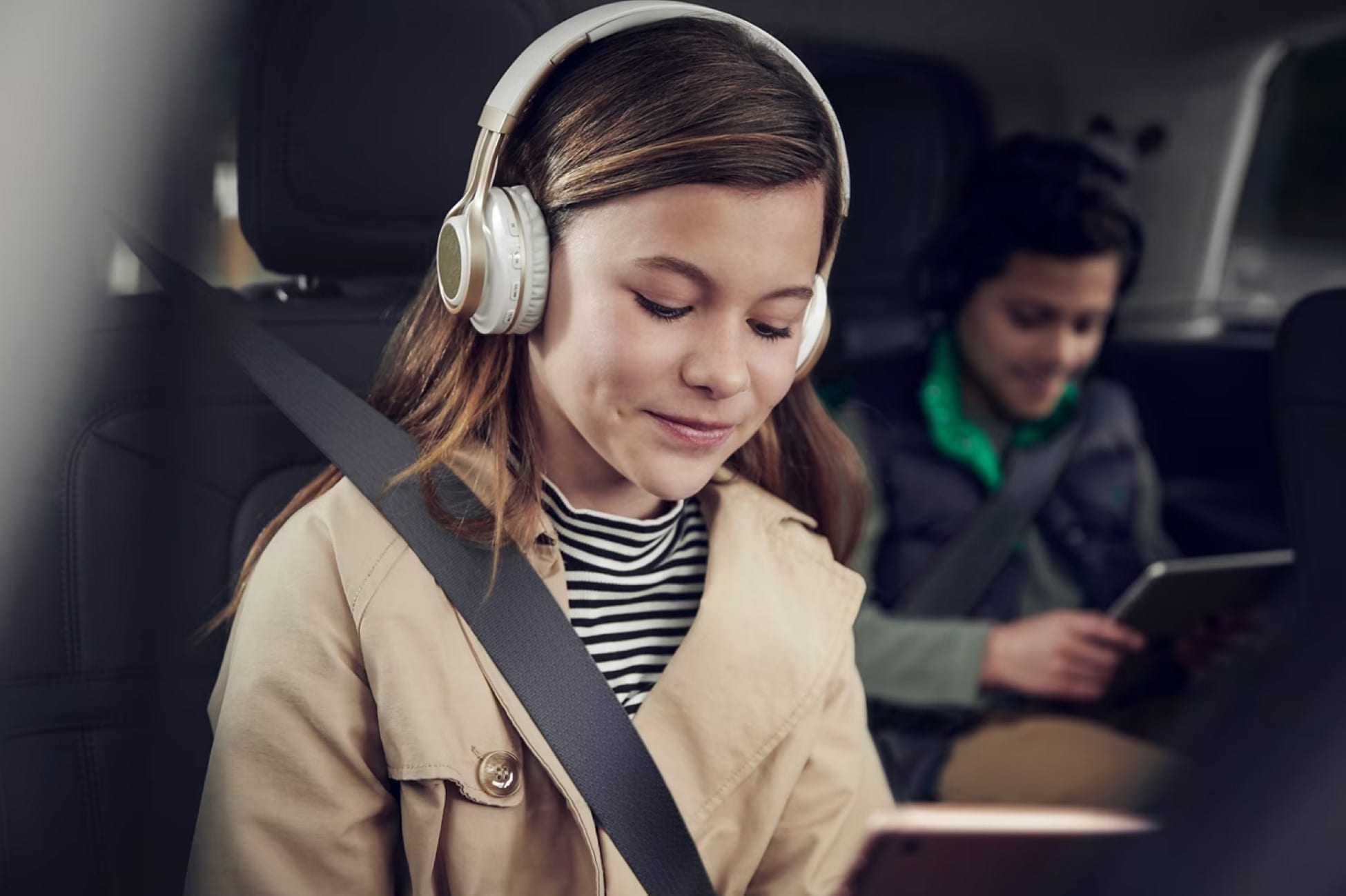 Two children are shown in the front and second-row seats of a Lincoln vehicle while looking at tablet devices and wearing headphones.