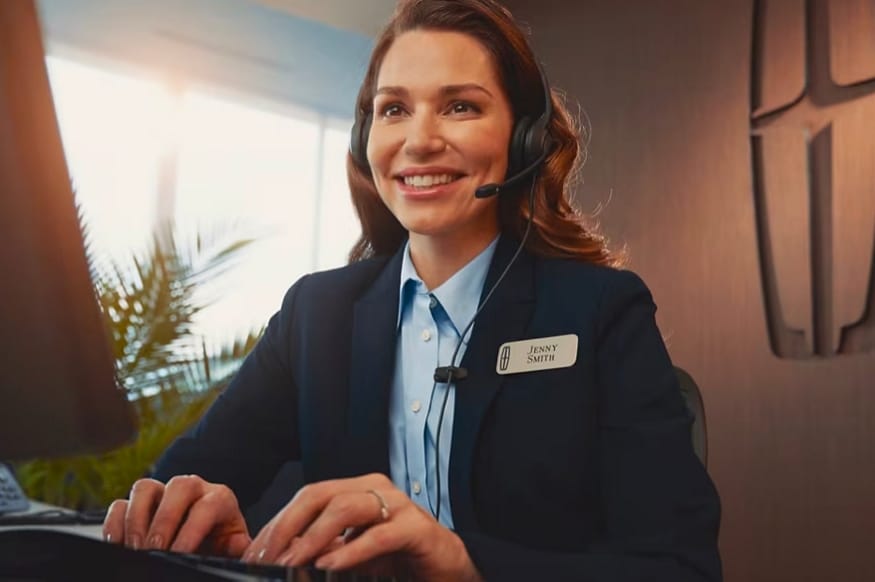 A woman is shown typing on keyboard while talking on a headset telephone.