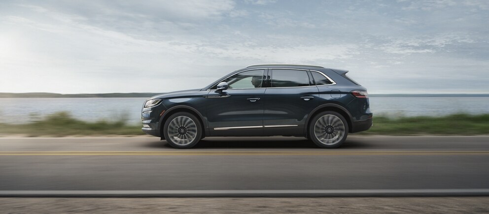 A 2021 Lincoln Nautilus is shown being driven on a lakeshore roadway