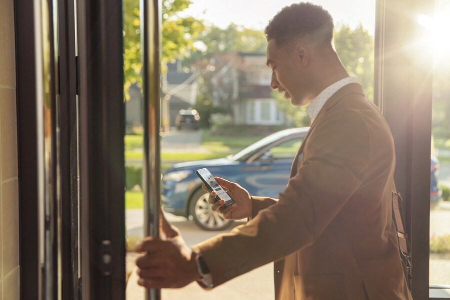A smartphone is being held in a man’s hand as he walks toward a 2022 Lincoln Nautilus in Flight Blue
