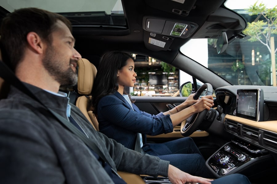 A couple is driving a 2022 Lincoln Corsair through the city during the day using Lincoln plus Alexa to find information