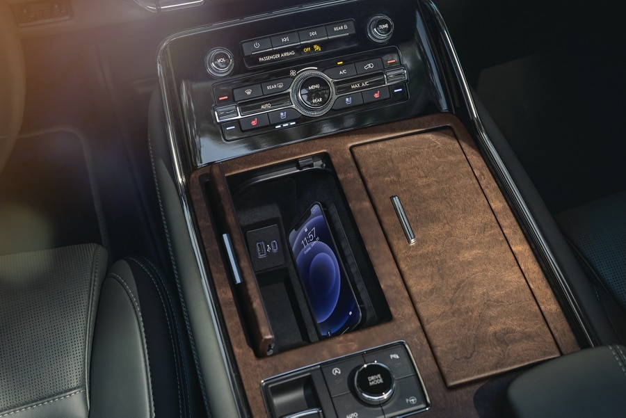 A smartphone is charging on the wireless charging pad that is tucked in a cubby integrated into the front center console