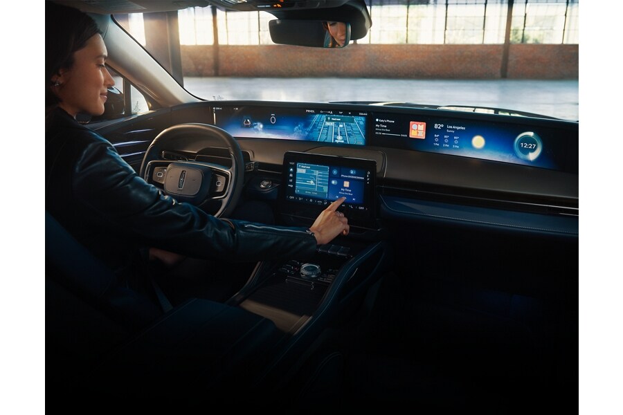 A woman is shown in the driver’s seat of a Lincoln Nautilus® SUV touching the center-stack display.