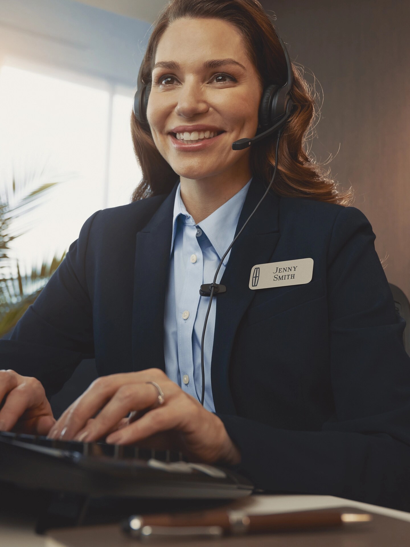 A support agent in a headset types at a desk with the Lincoln logo visible in the background