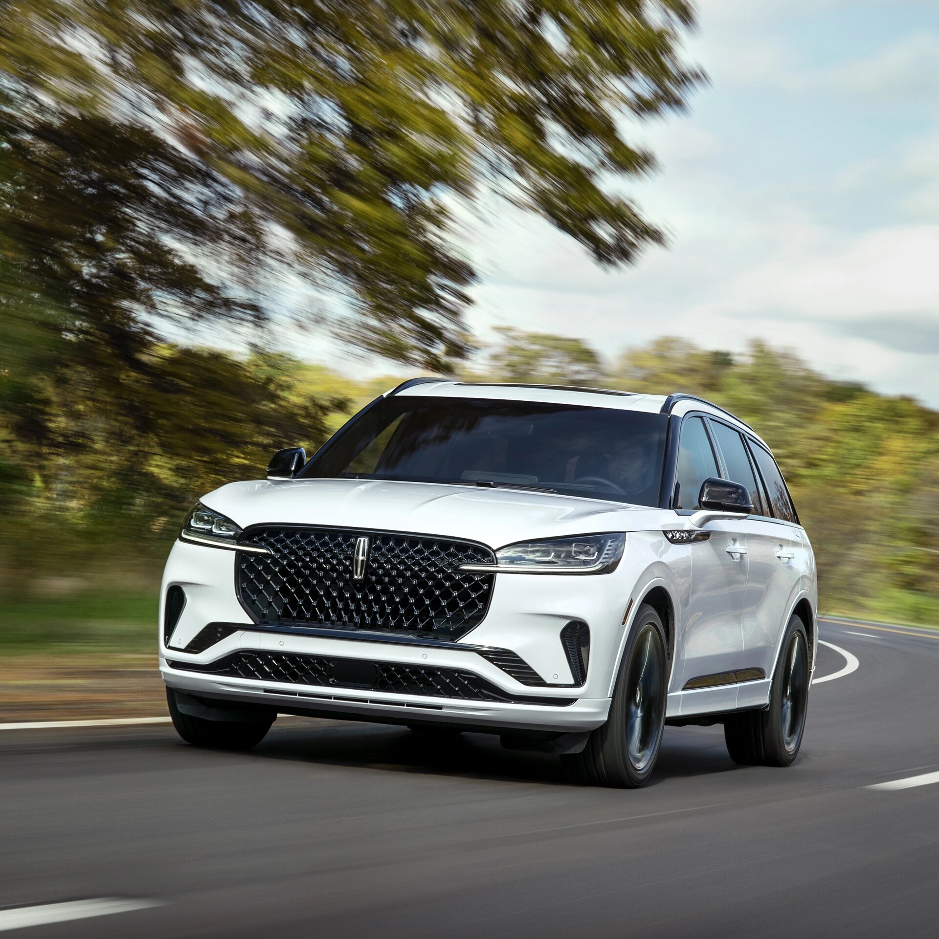 A 2026 Lincoln Aviator® SUV is shown driving on a tree-lined road
