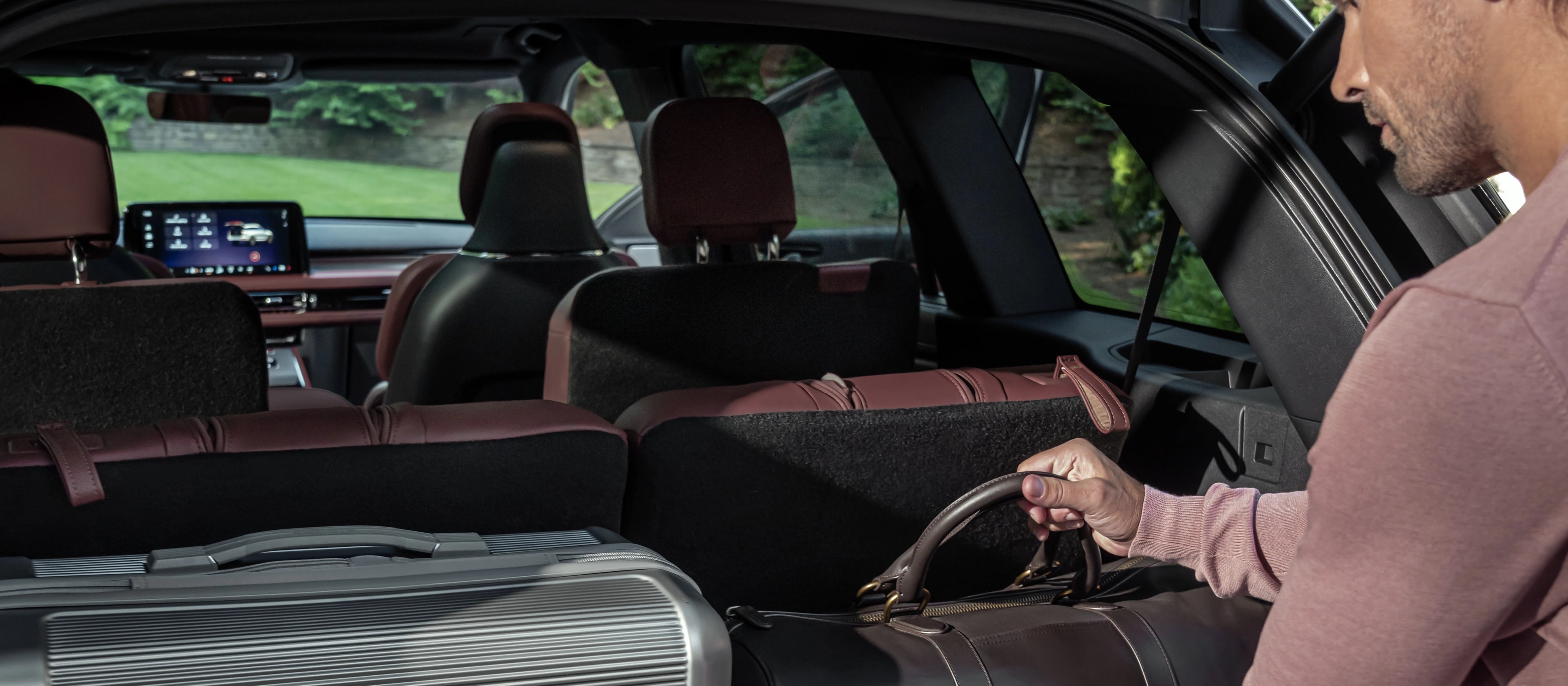 A person loads a leather bag into the rear cargo area of a 2026 Lincoln Aviator