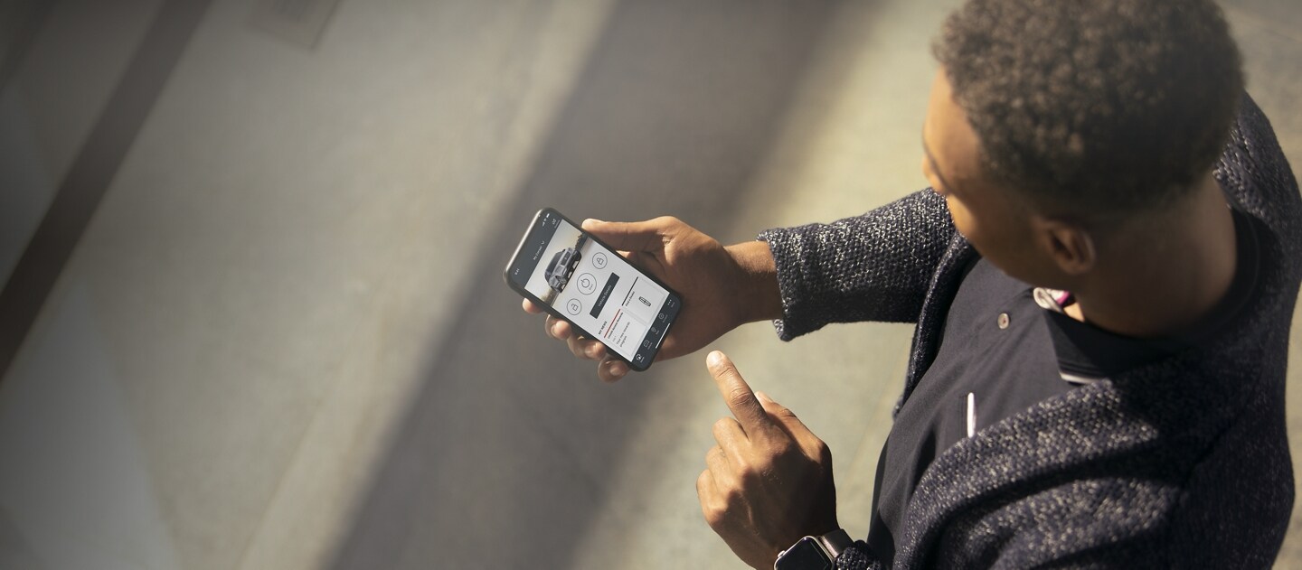 A man is standing at a sunny window interacting with the Lincoln Way app on his smartphone device