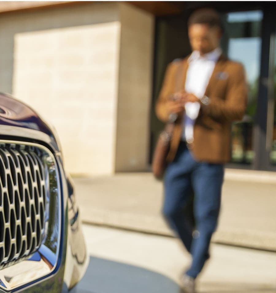 A man is shown approaching a Lincoln vehicle as he uses his smartphone