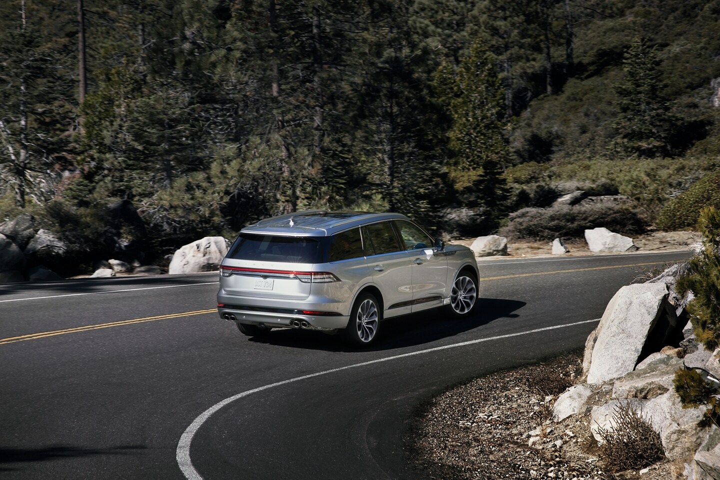 A 2023 Lincoln Aviator® is shown being driven on a winding road as it approaches a speed limit sign